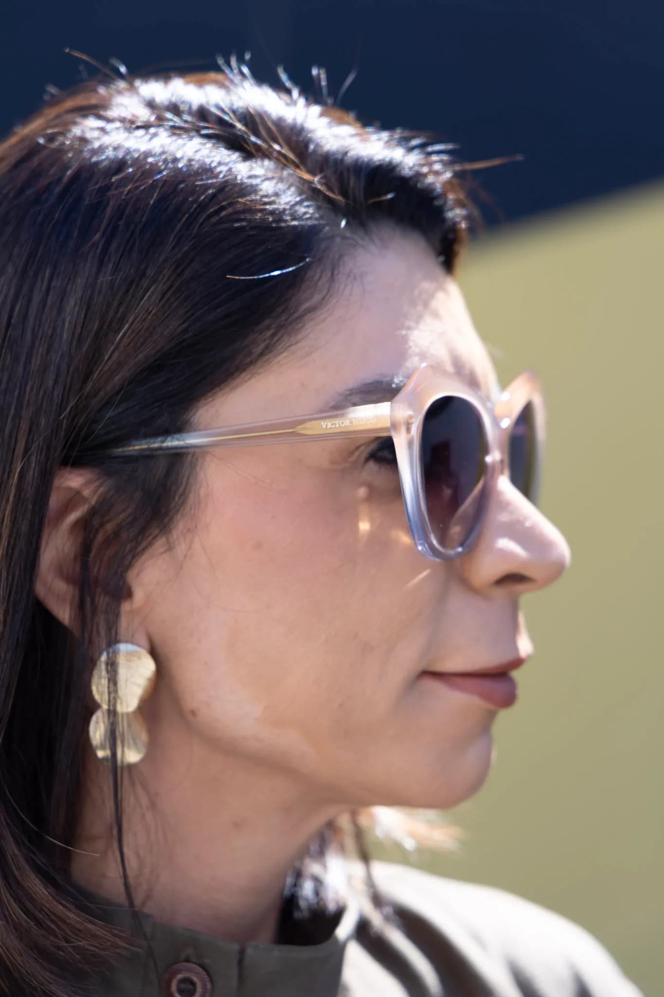Close de modelo da Ótica CAP de perfil com óculos de sol de lente clara e brinco dourado.