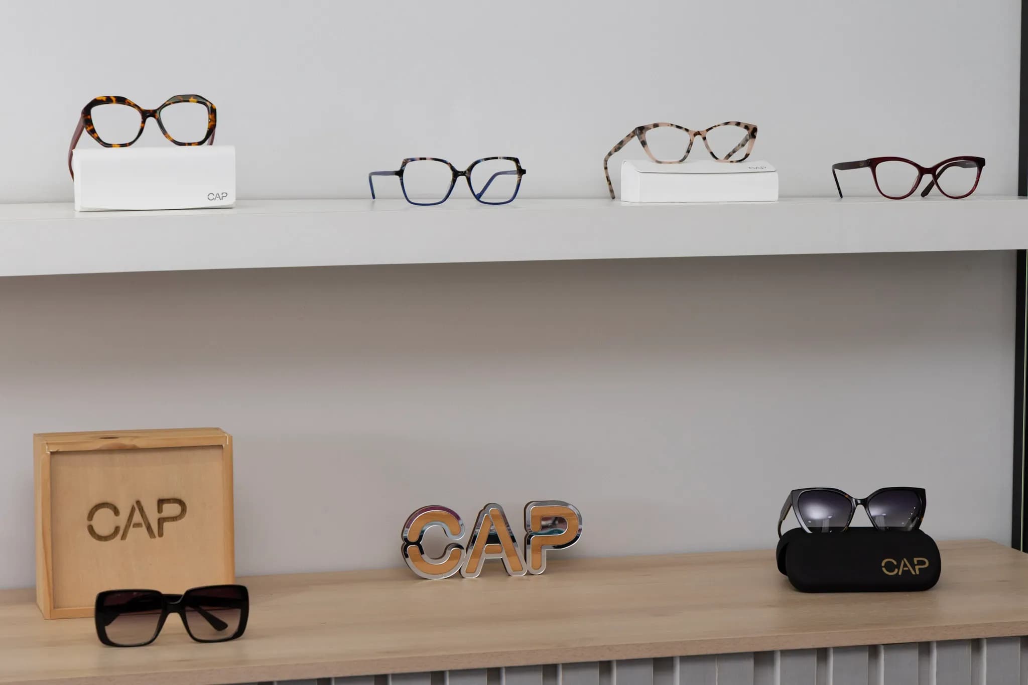 Vitrine da Ótica CAP com armações CAP nas prateleiras, letreiro CAP e caixa de madeira com a marca.